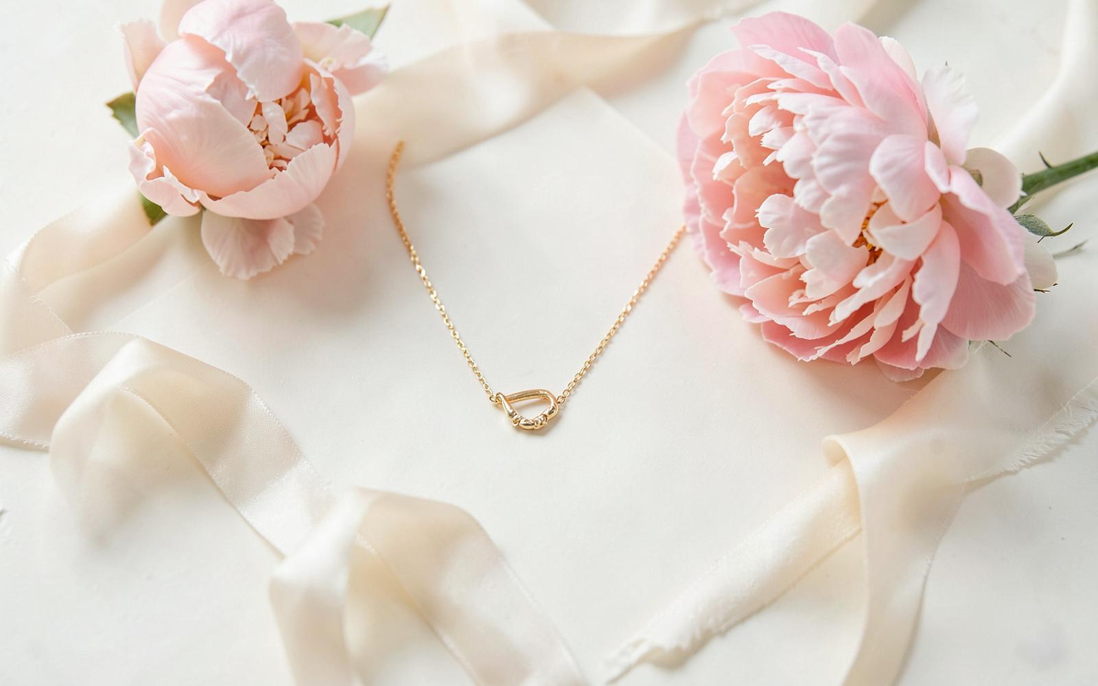 Gold necklace, blush peonies and ivory silk ribbon arranged as a romantic gift flat lay